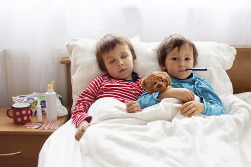 Two sick boys, brothers, lying down in bed with fever