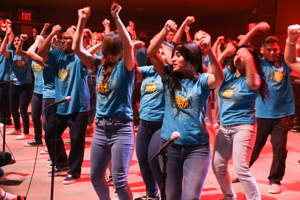 A group of teens dance on stage while bathed in a red light